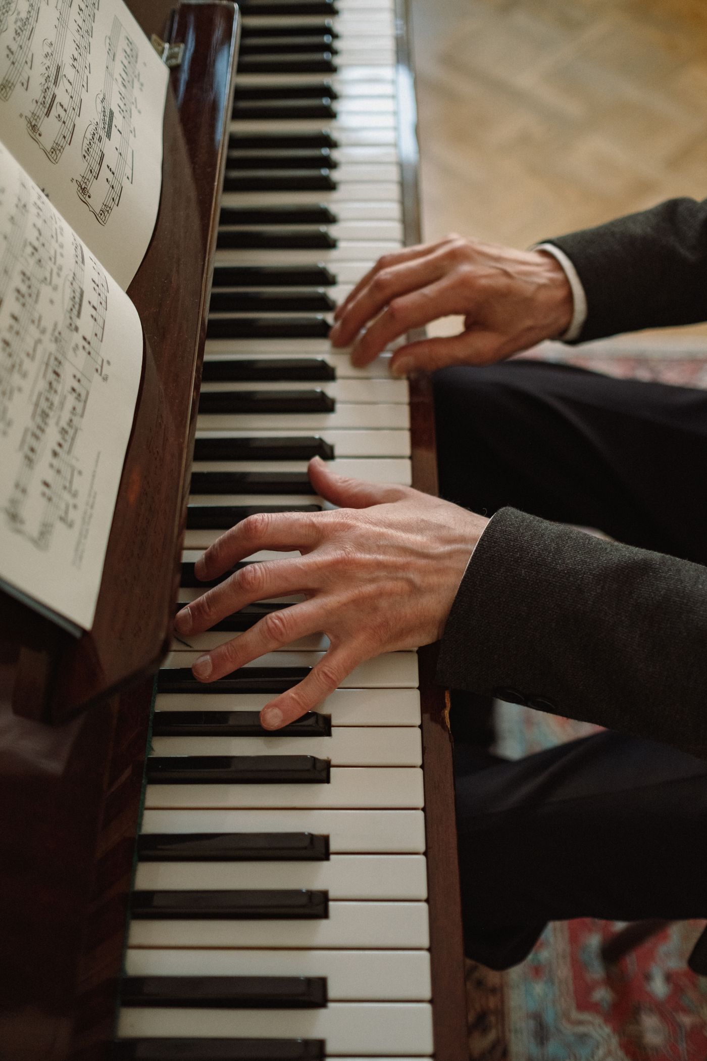 A close view of hands playing piano keys beside sheet music