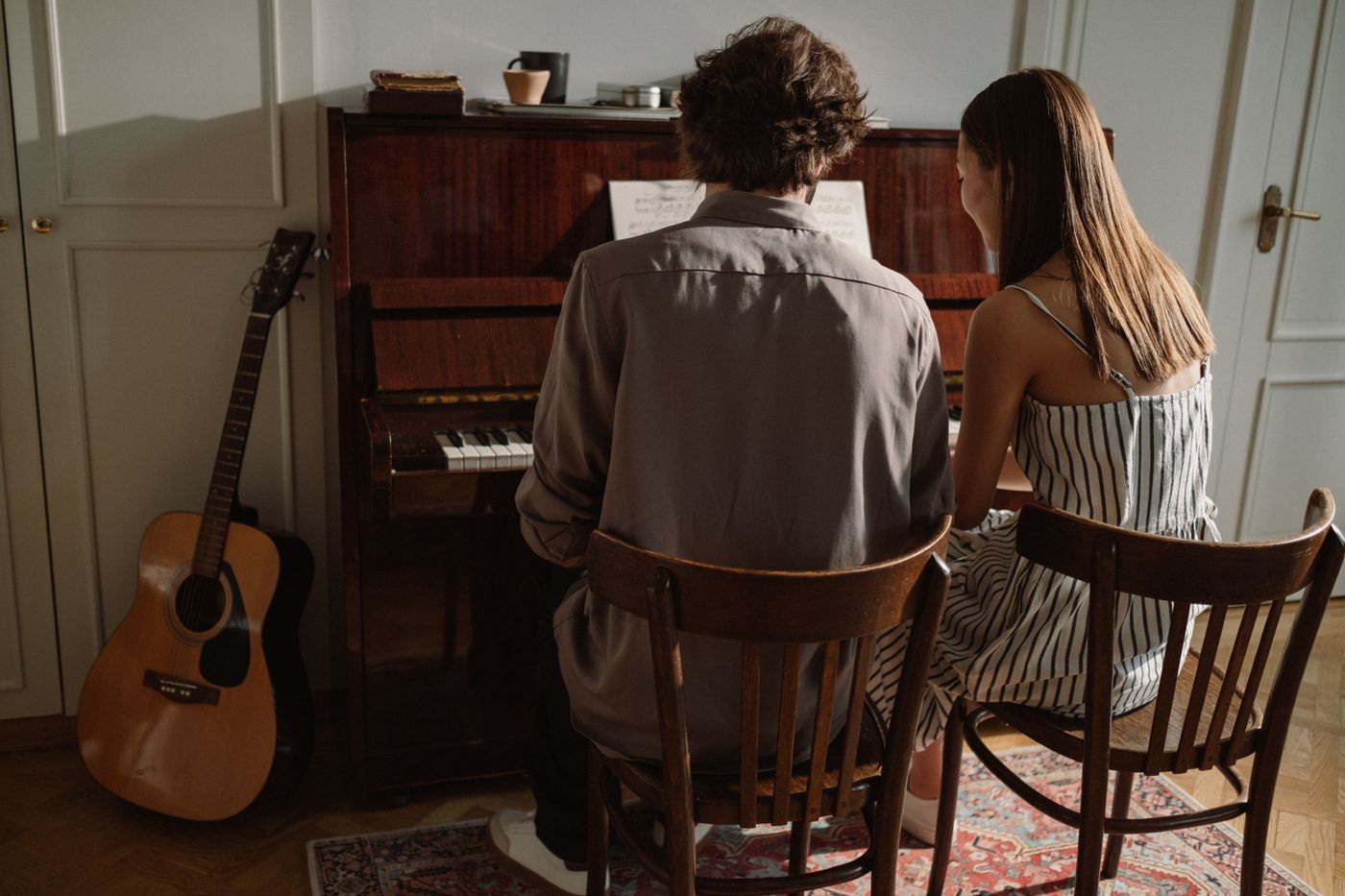 Two people playing piano together with a guitar nearby