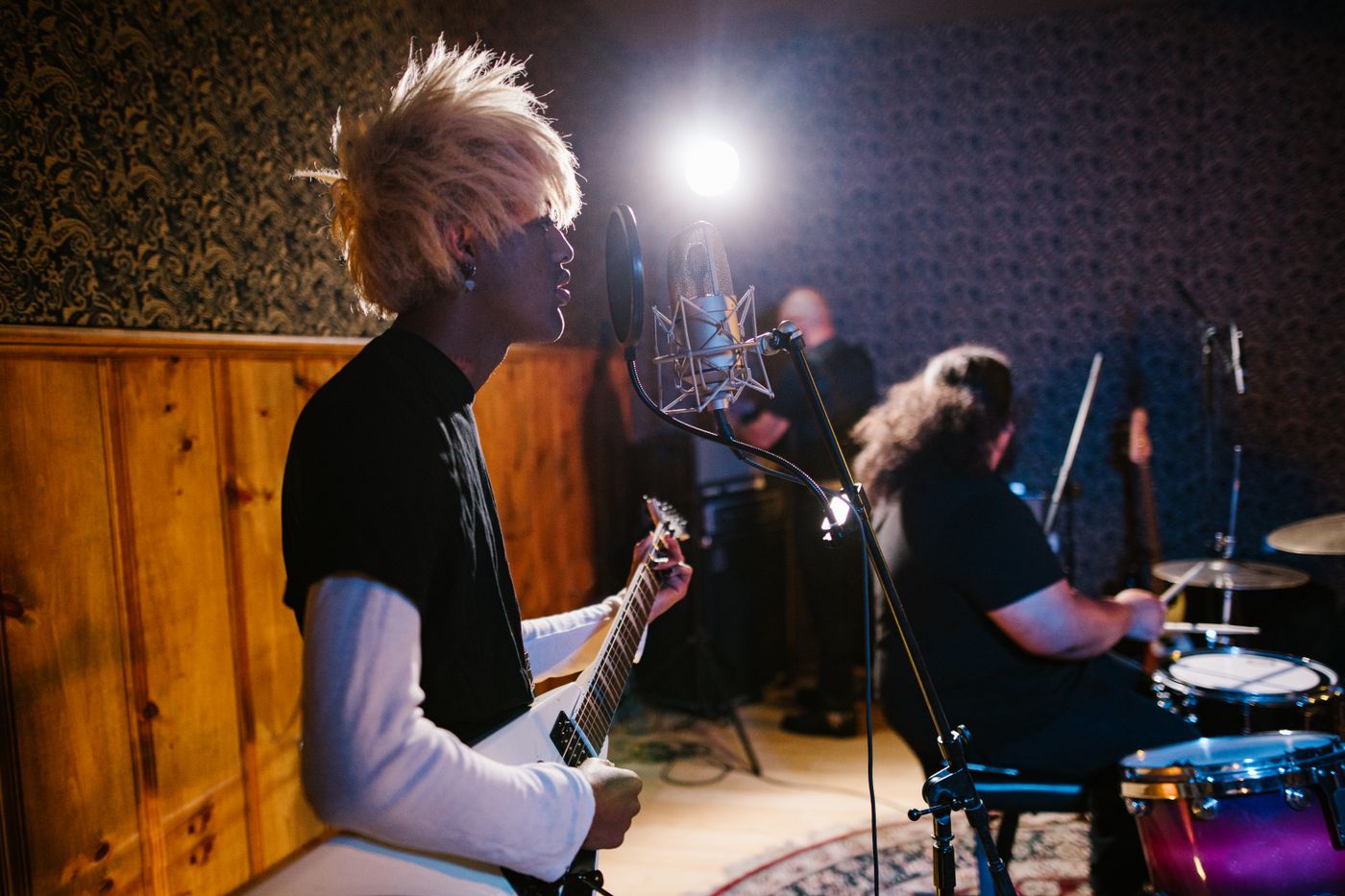 A singer playing electric guitar with a drummer behind him